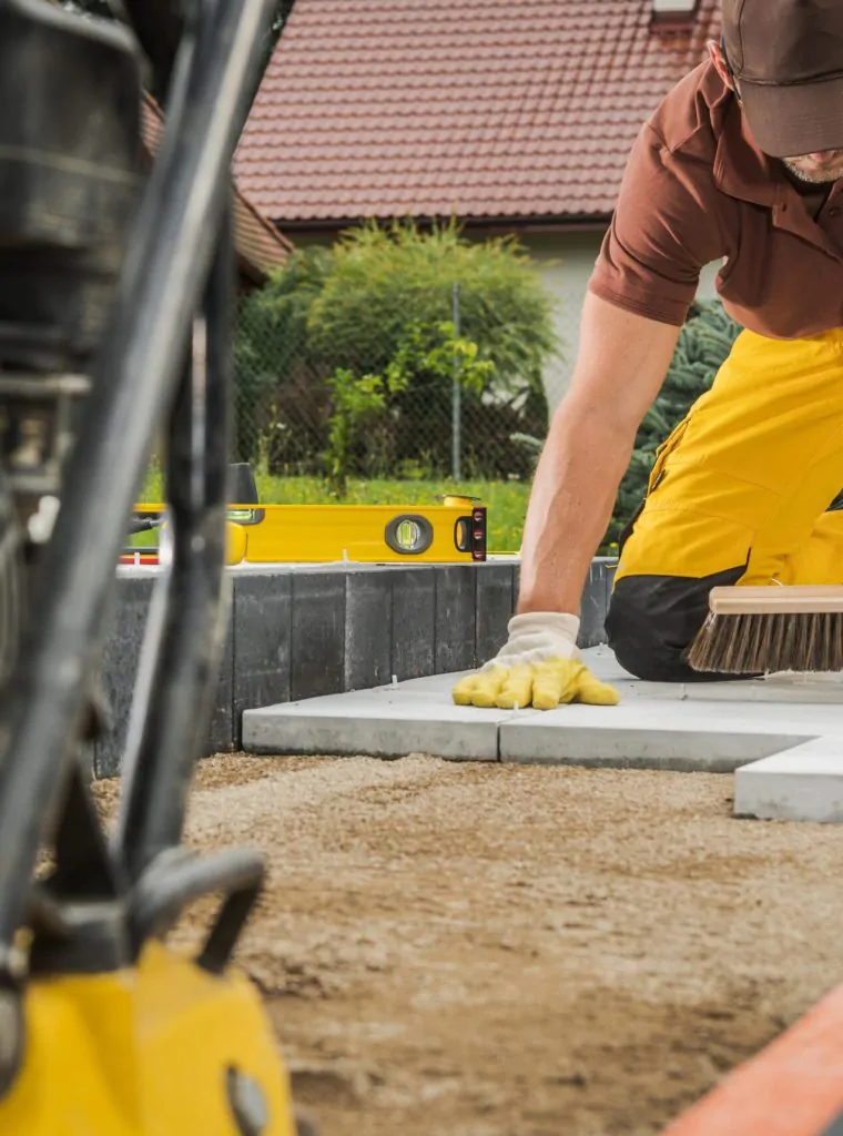 Residential Pathway Concrete Bricks Paving by Caucasian Worker. Compacting Machine in a Front.